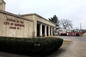 Firehouse #1 is a brown concrete building with four garage doors for fire trucks. A firetruck is seen the the background.